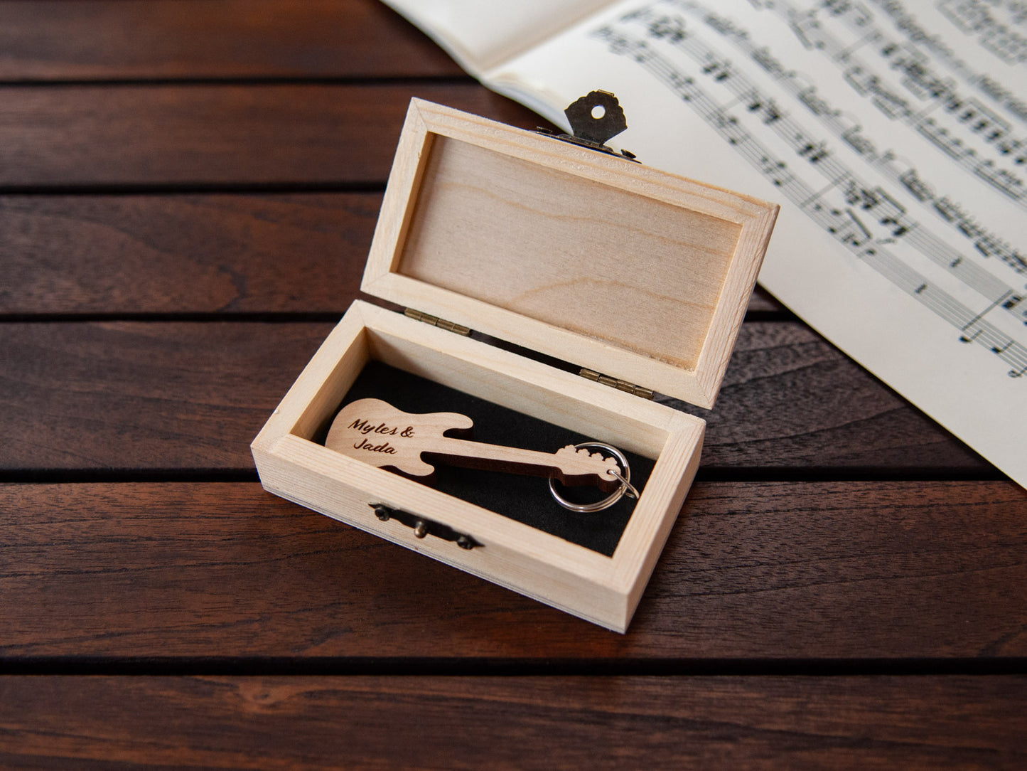 A keychain in the shape of a bass guitar stored in a small wooden box, featuring custom engraving.