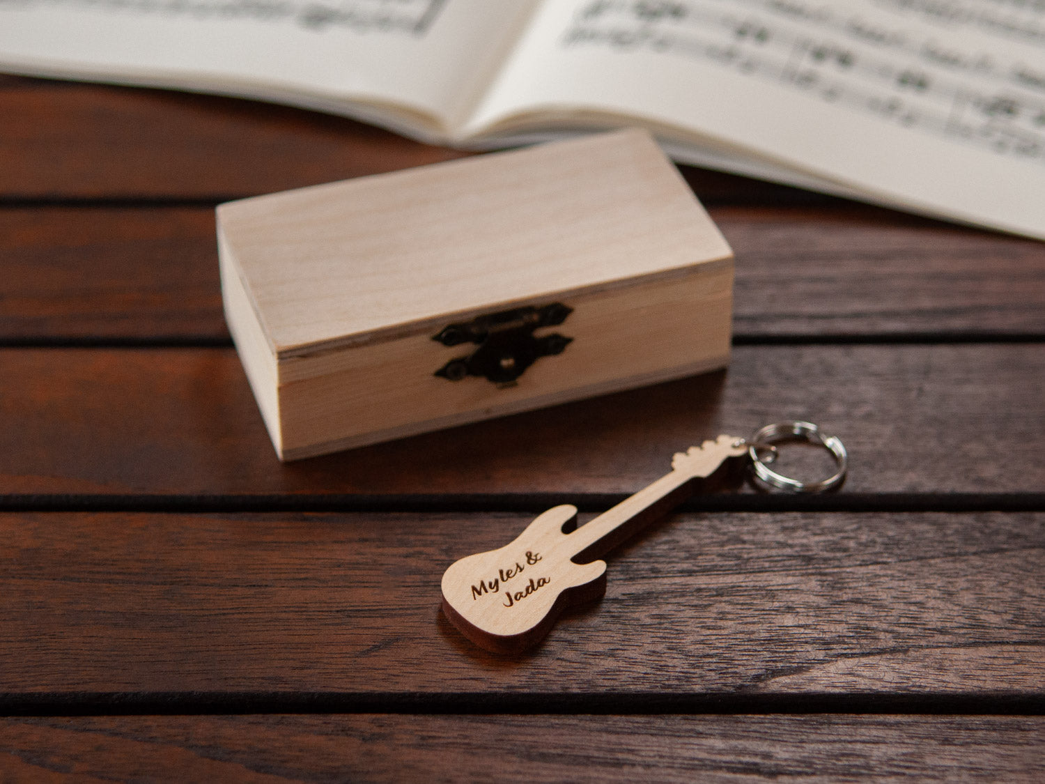 A keychain in the shape of a bass guitar in front of a small wooden box, with custom engraving.