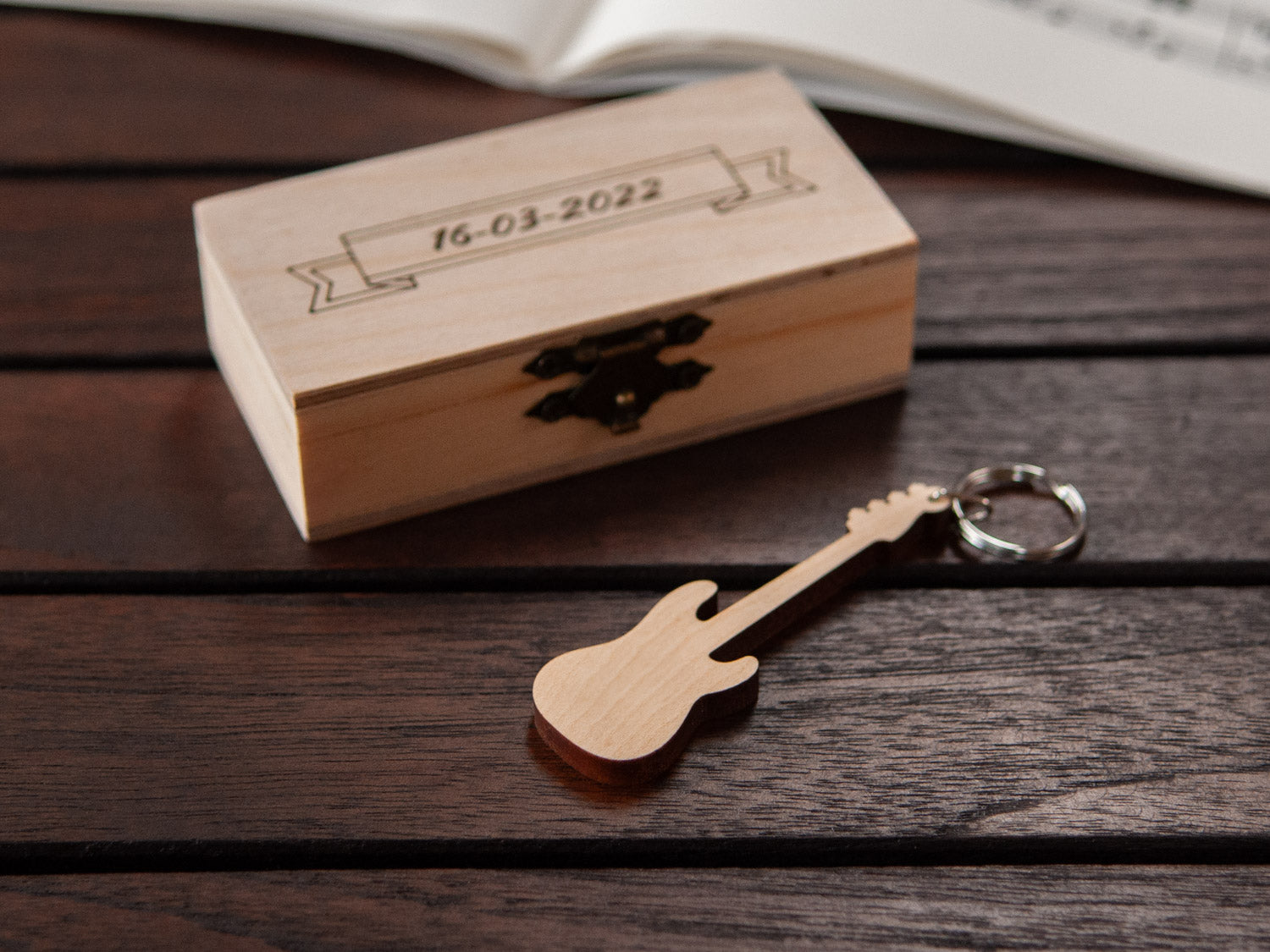 A bass guitar shaped keychain in front of a small engraved wooden box