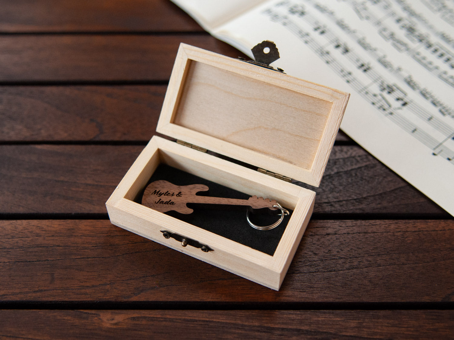 A keychain in the shape of a bass guitar stored in a small wooden box, featuring custom engraving.