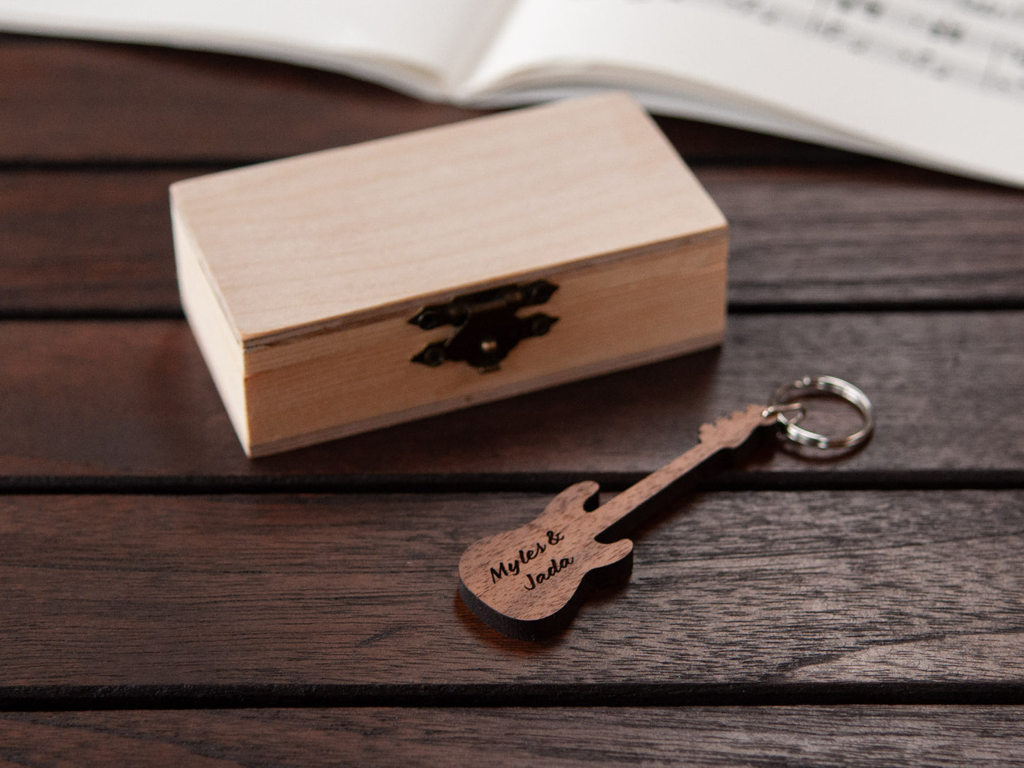 A keychain in the shape of a bass guitar with custom engraving, in front of a small wooden box