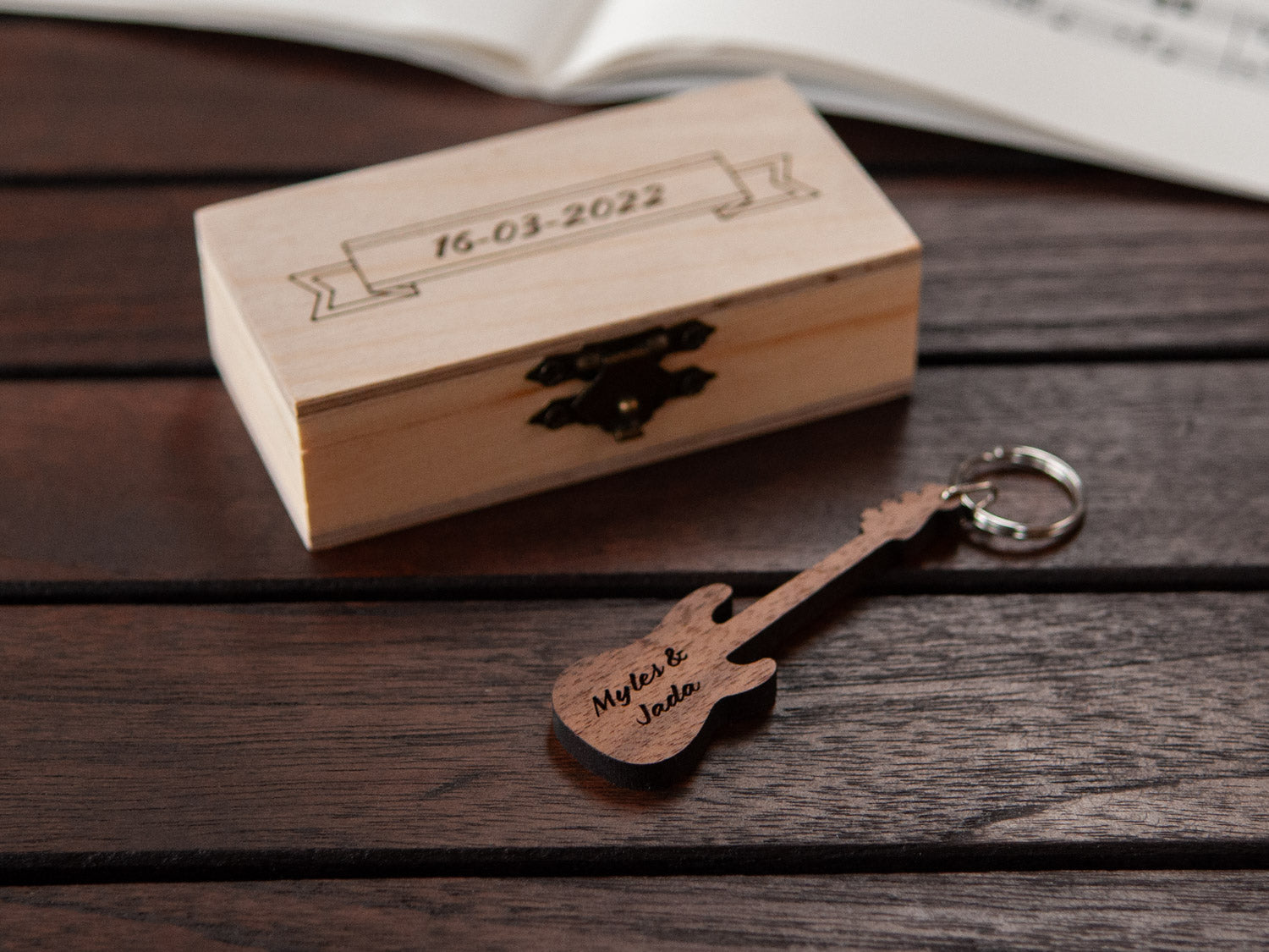 A keychain in the shape of a bass guitar in front of a small wooden box, with custom engraving.