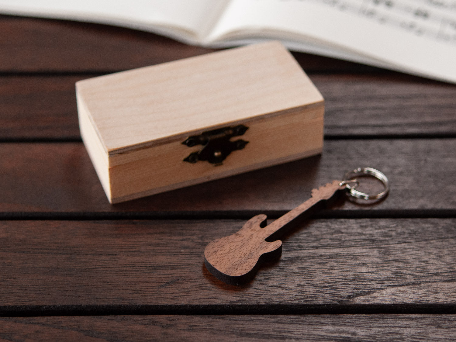 A keychain in the shape of a bass guitar  made from walnut, in front of a small wooden box