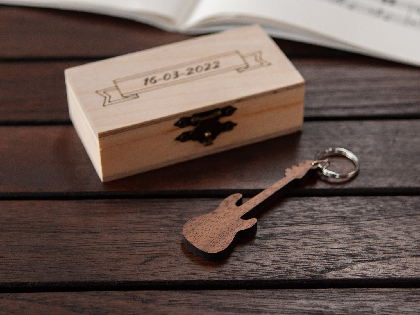 A keychain in the shape of a bass guitar in front of a small wooden box, with custom engraving.