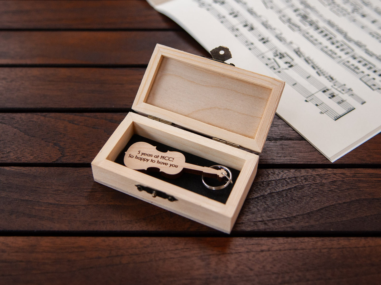 A keychain in the shape of a cello stored in a small wooden box, featuring custom engraving.