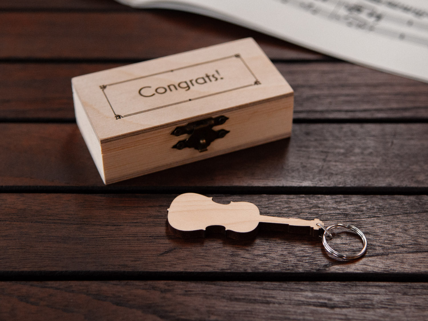 Keychain in the shape of a cello in front of a small wooden box, with custom engraving.