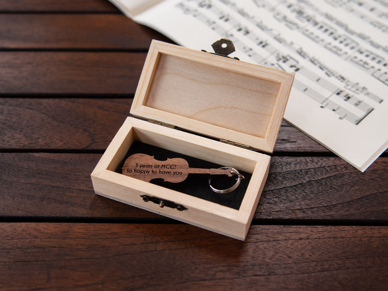 A keychain in the shape of a cello stored in a small wooden box, featuring custom engraving.