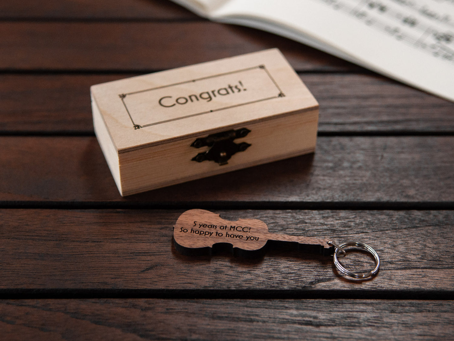 Keychain in the shape of a cello in front of a small wooden box, with custom engraving.