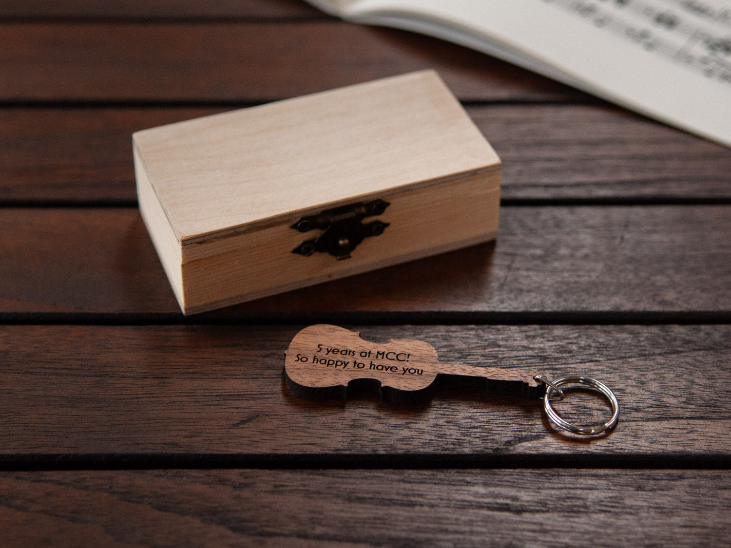 An engraved cello shaped keychain in front of a small wooden box