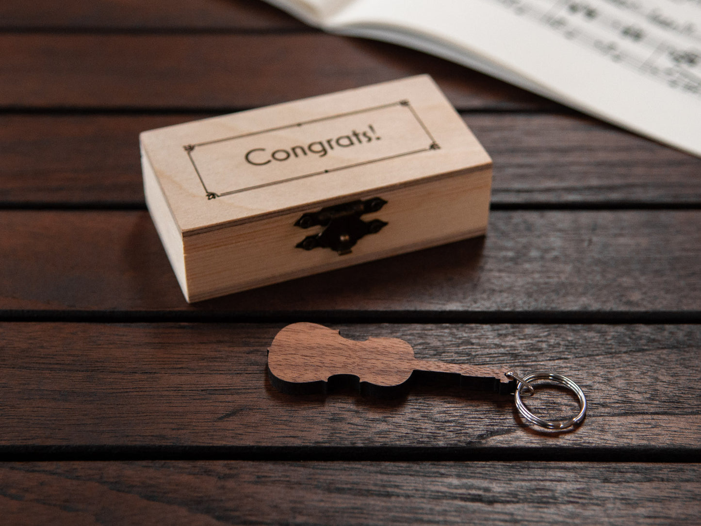 A cello shaped keychain in front of a small engraved wooden box