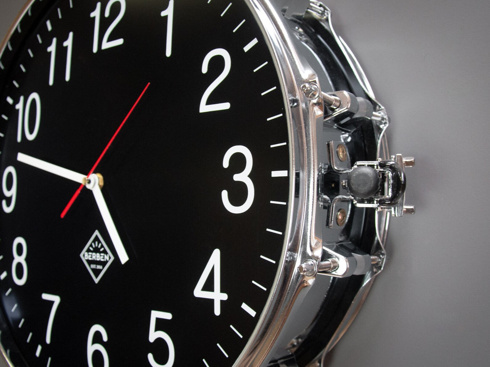 Detail of a clock made from a drum with a black clock face. The shell and rims have a chrome finish.