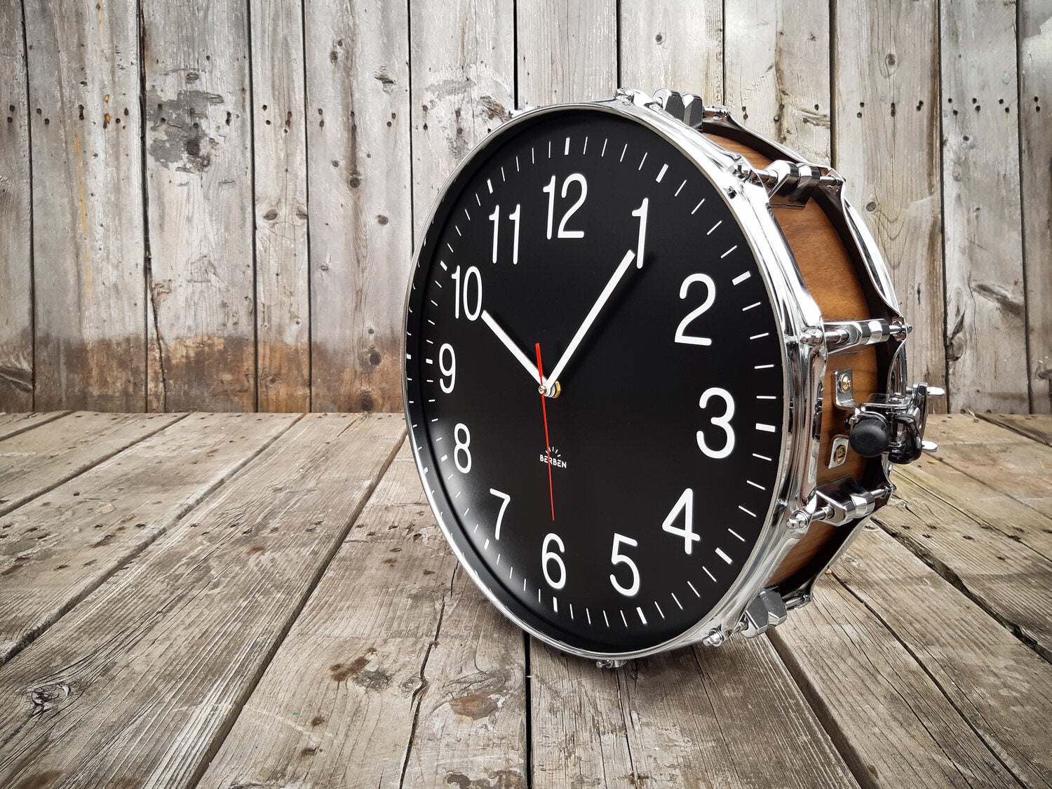 A clock made from a drum with a black clock face. The shell is finished with a rich walnut veneer.