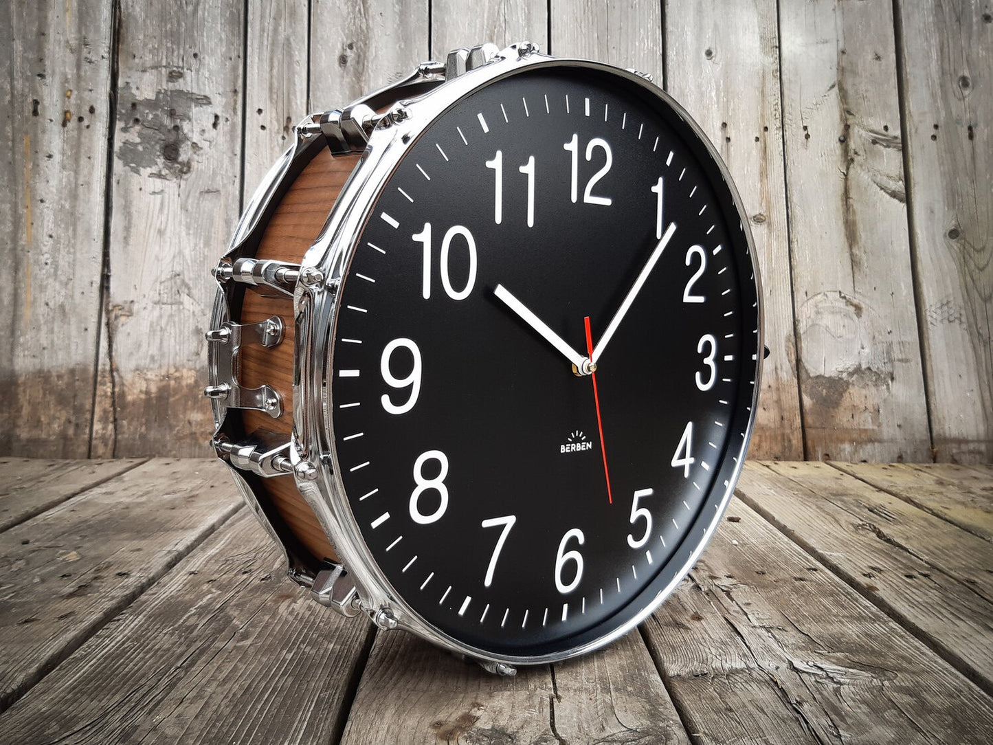 A clock made from a drum with a black clock face. The shell is finished with a rich walnut veneer.