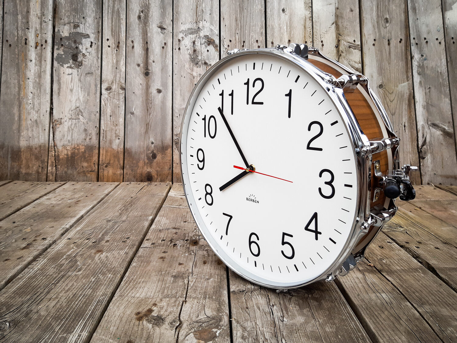 A clock made from a drum with a white clock face. The shell is finished with a rich walnut veneer.