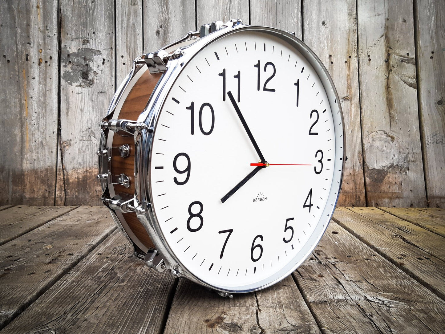 A clock made from a drum with a white clock face. The shell is finished with a rich walnut veneer.