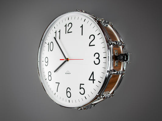 A clock made from a drum with a white clock face. The shell is finished with a rich walnut veneer.