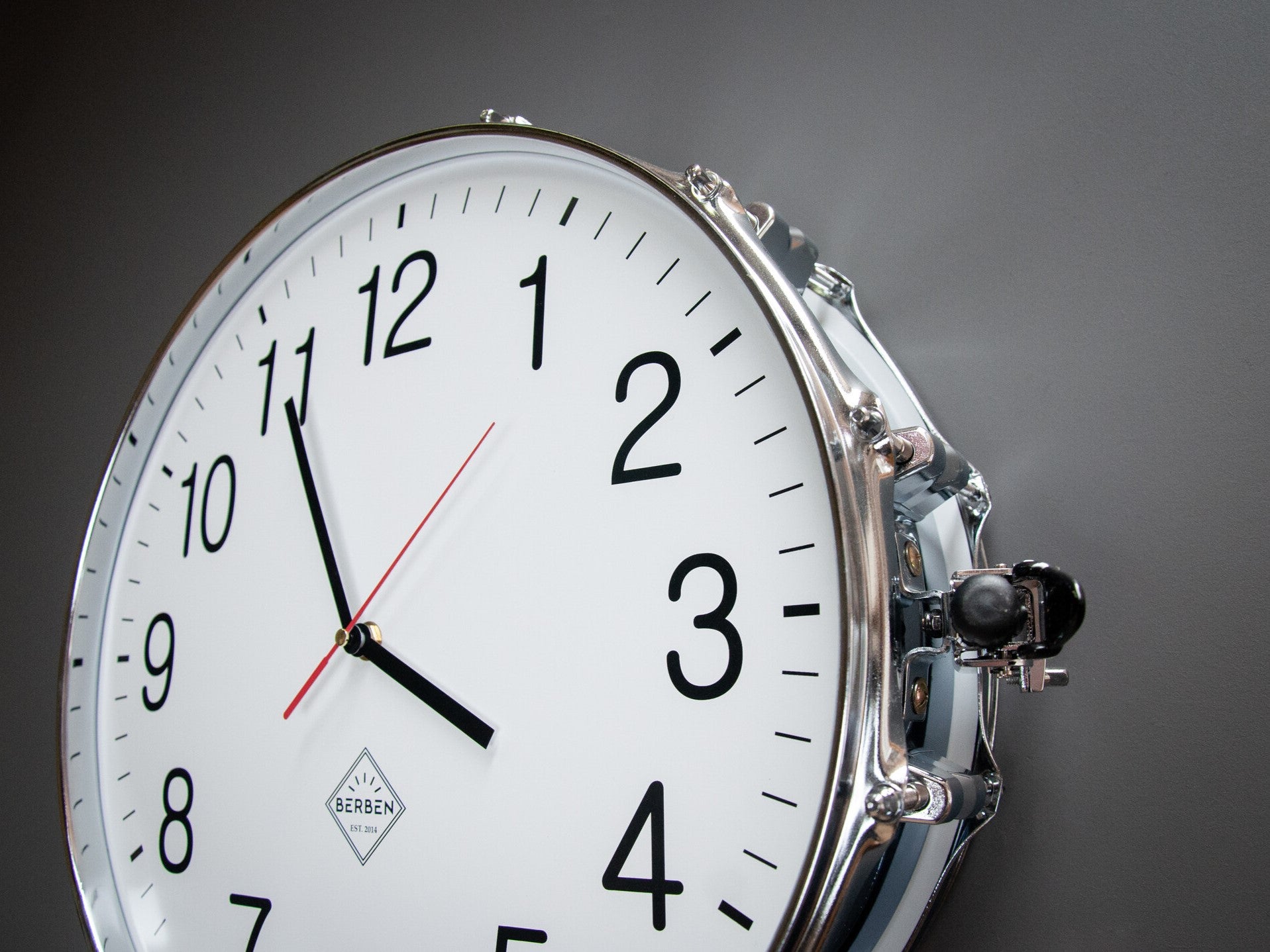 Details of a clock made from a drum with a white clock face. The shell and rims have a chrome finish.