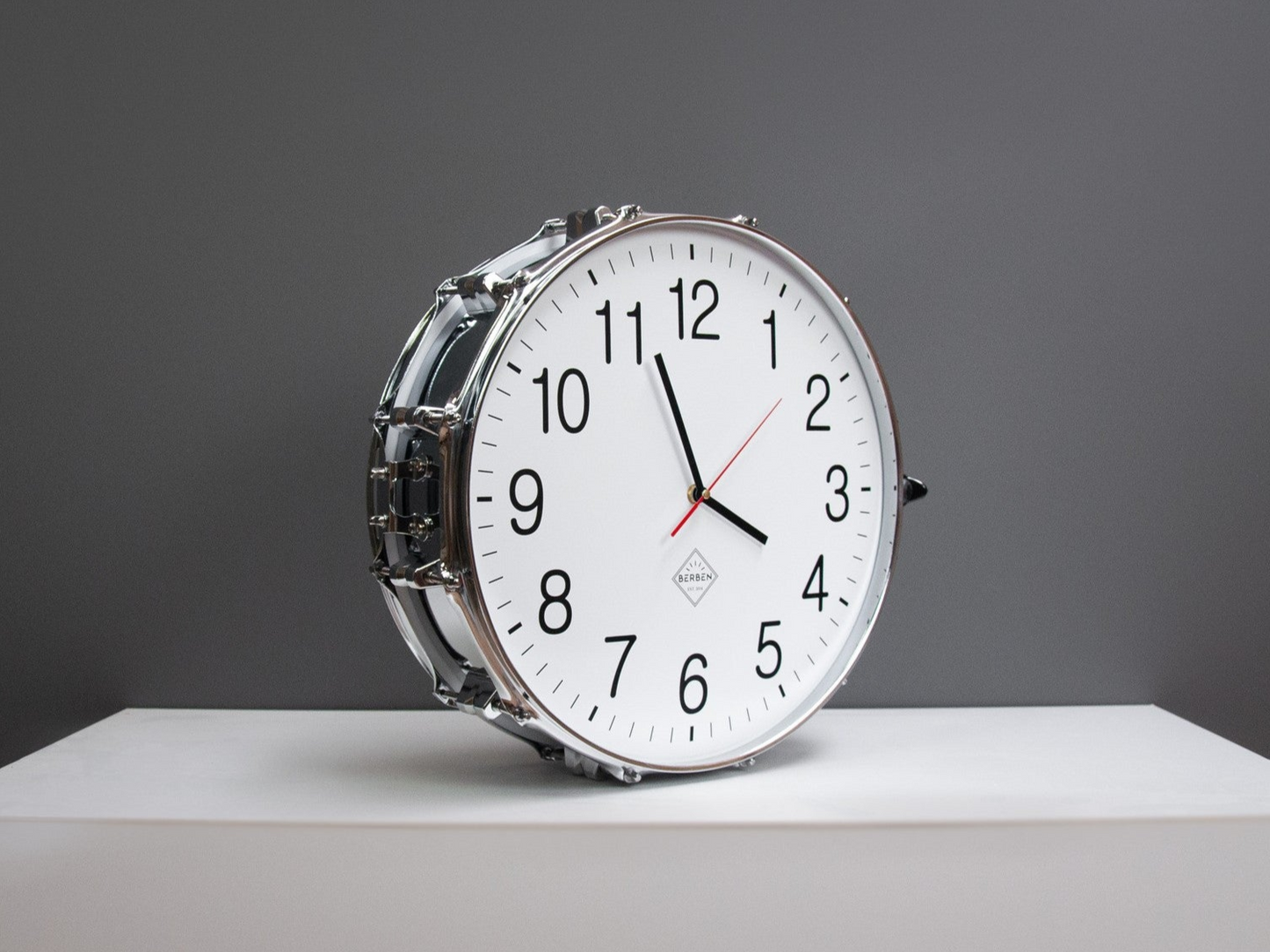 A clock made from a drum with a white clock face. The shell and rims have a chrome finish.