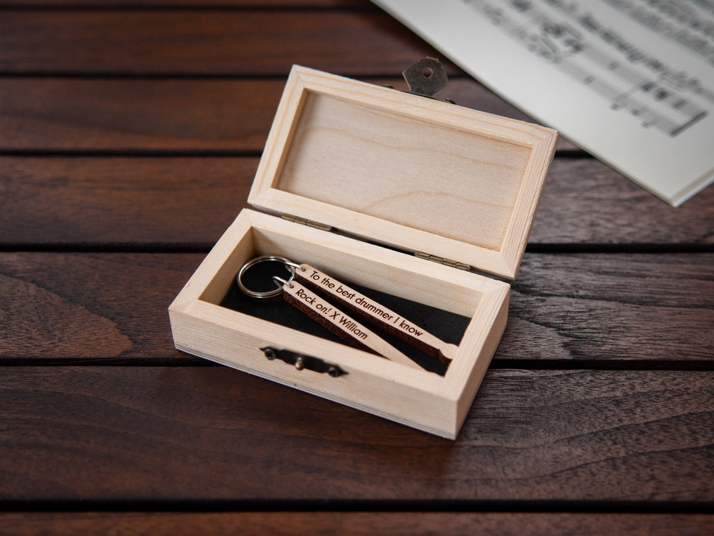 A keychain in the shape of drumsticks stored in a small wooden box, featuring custom engraving.