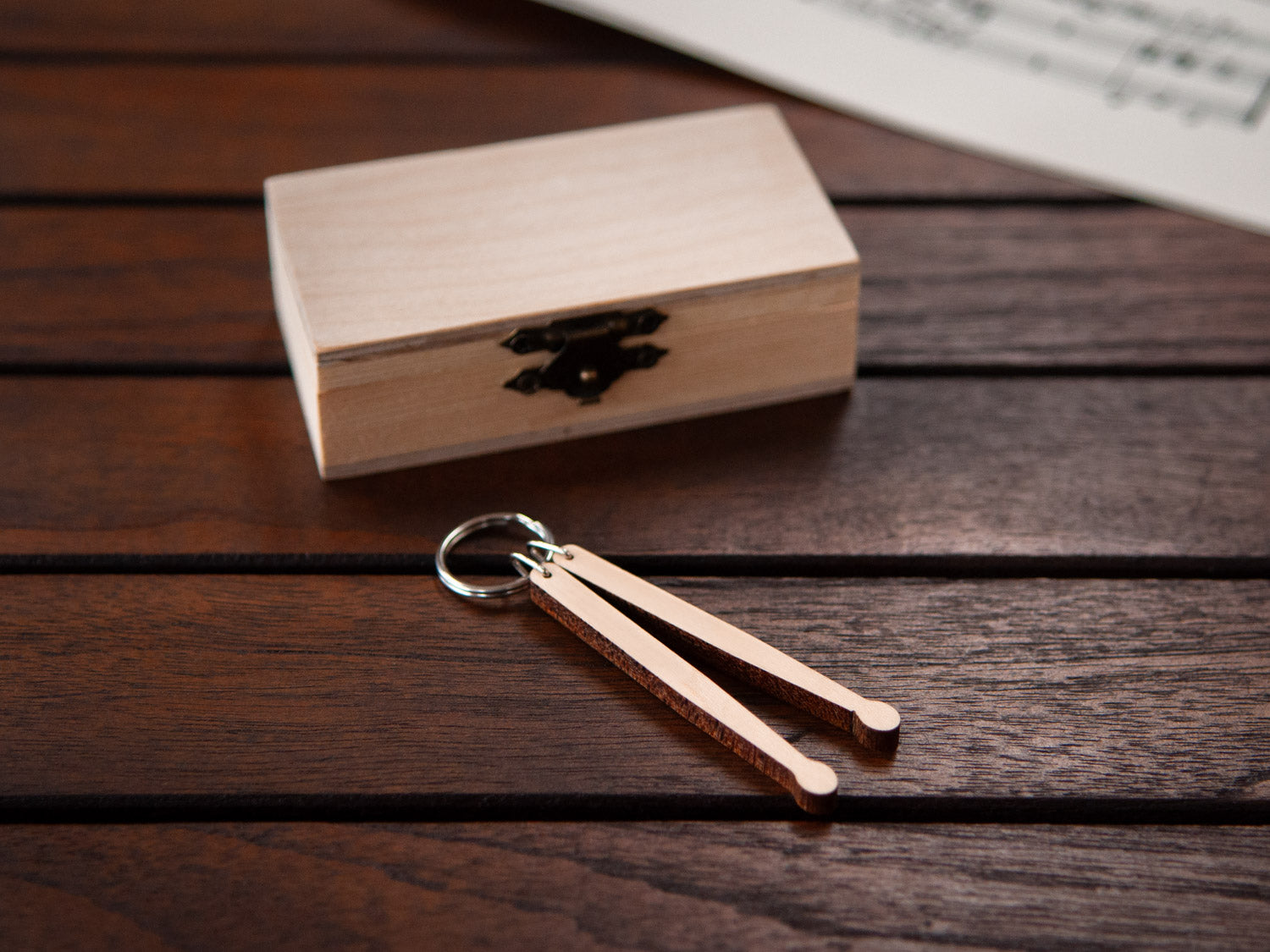 A keychain in the shape of a pair of drumsticks, in front of a small wooden box