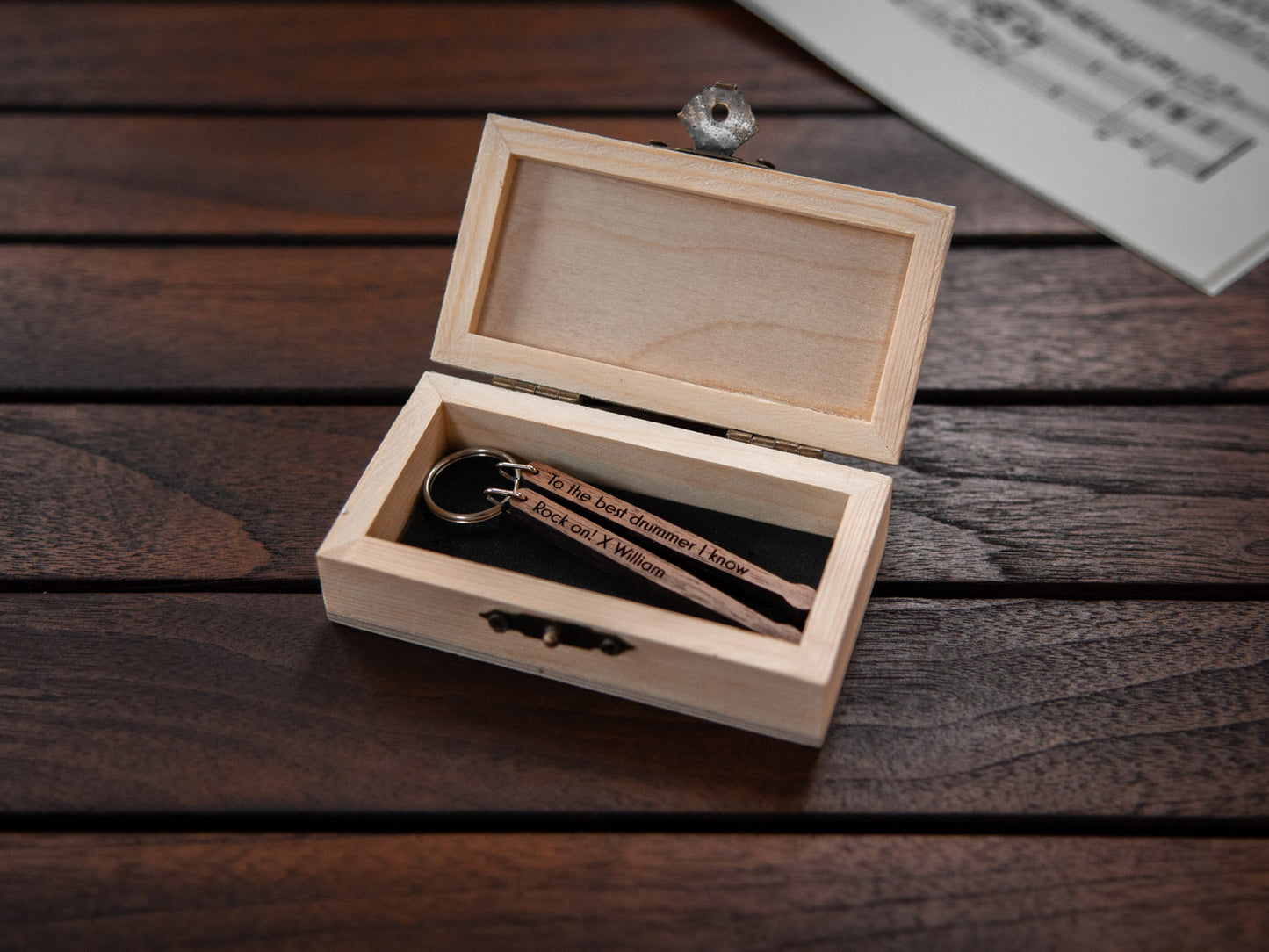 A keychain in the shape of drumsticks stored in a small wooden box, featuring custom engraving.