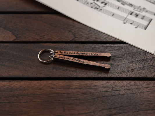 A drumsticks shaped keychain made from walnut wood, with personalized engraving