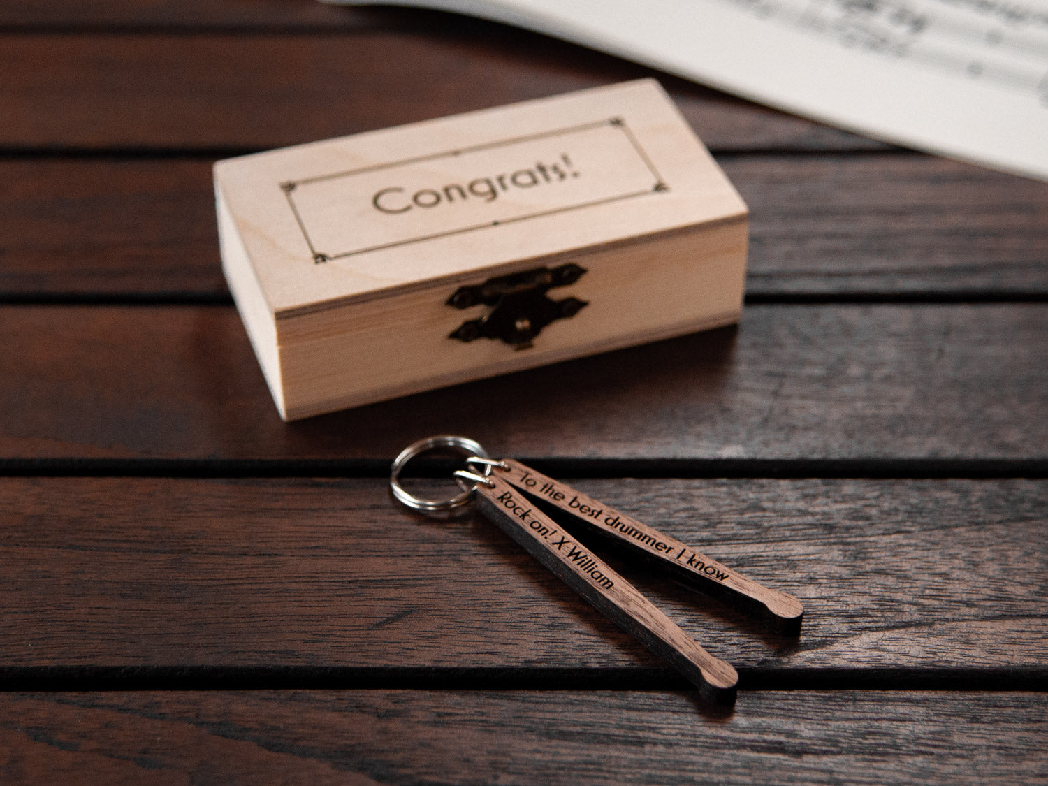 A keychain in the shape of drumsticks, stored in a small wooden box, featuring custom engraving.