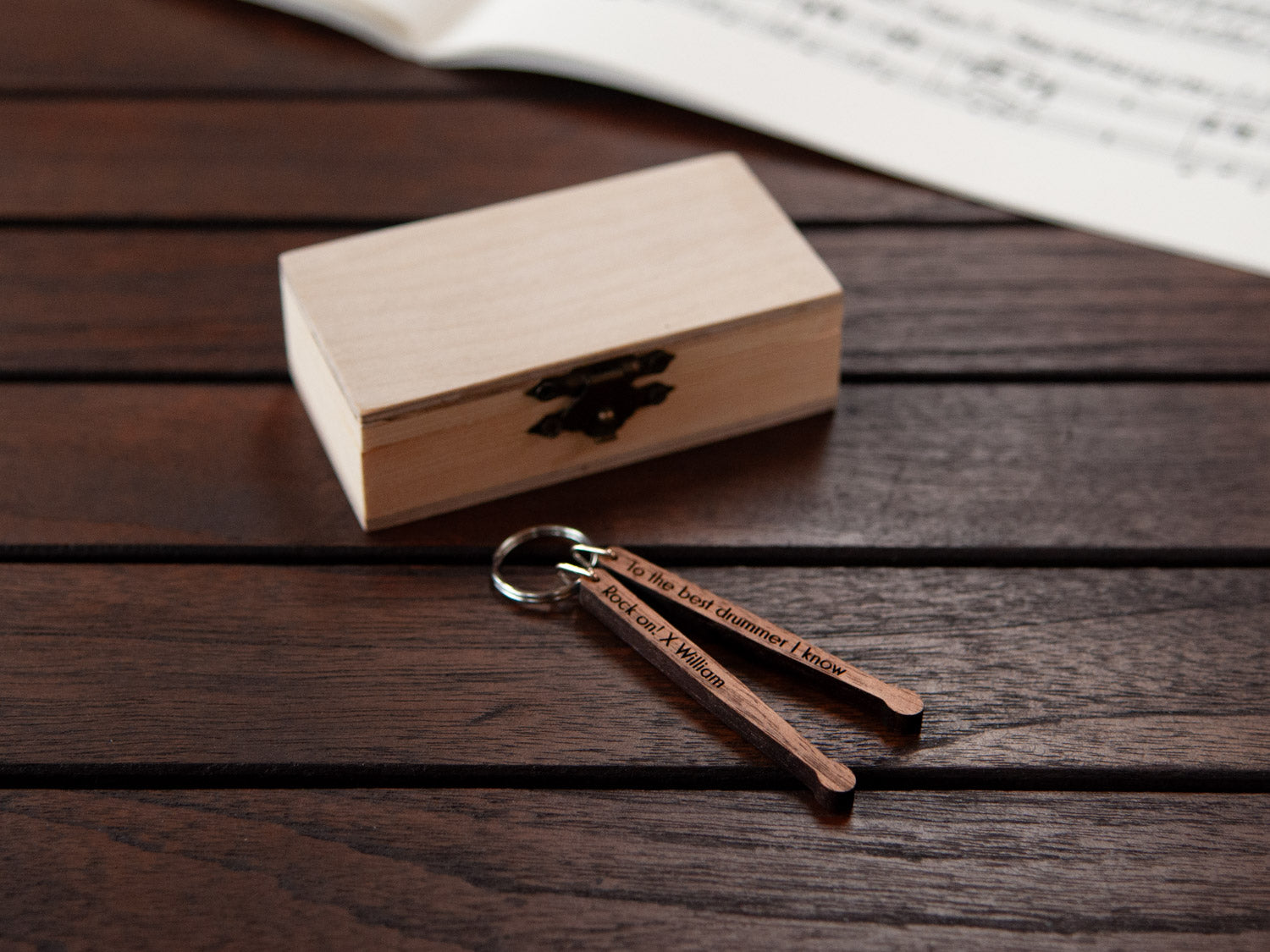 A keychain in the shape of a pair of drumsticks, in front of a small wooden box