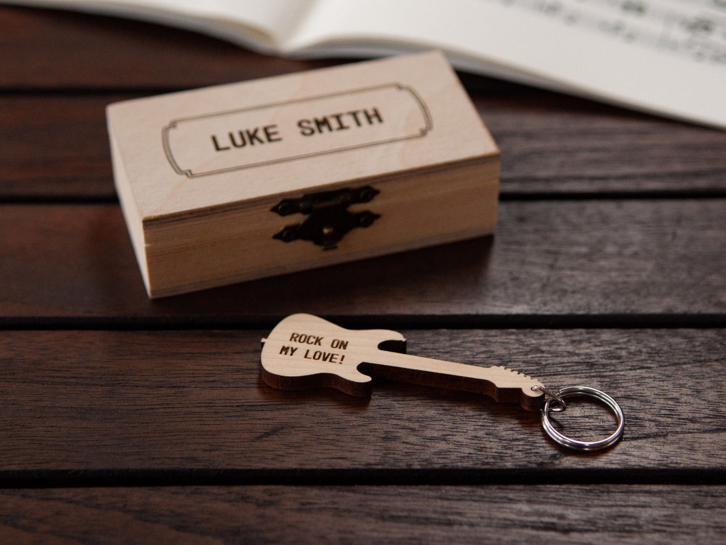 Electric guitar keychain displayed in front of a small wooden box, with a custom engraving.