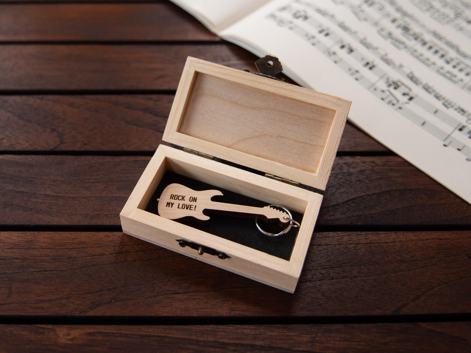 Electric guitar shaped keychain placed inside a compact wooden box, featuring a custom engraving.