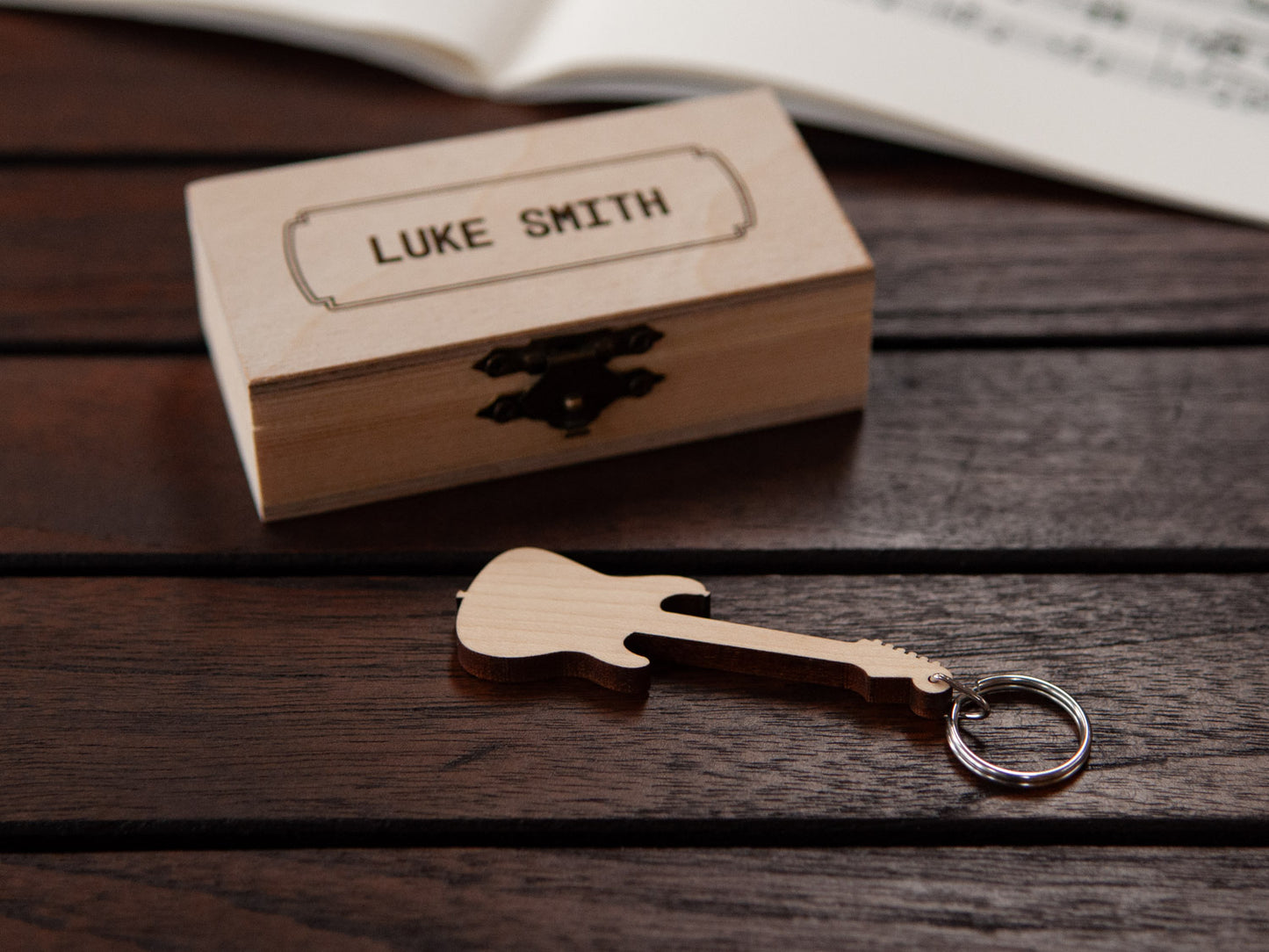 Electric guitar keychain displayed in front of a small wooden box, with a custom engraving.