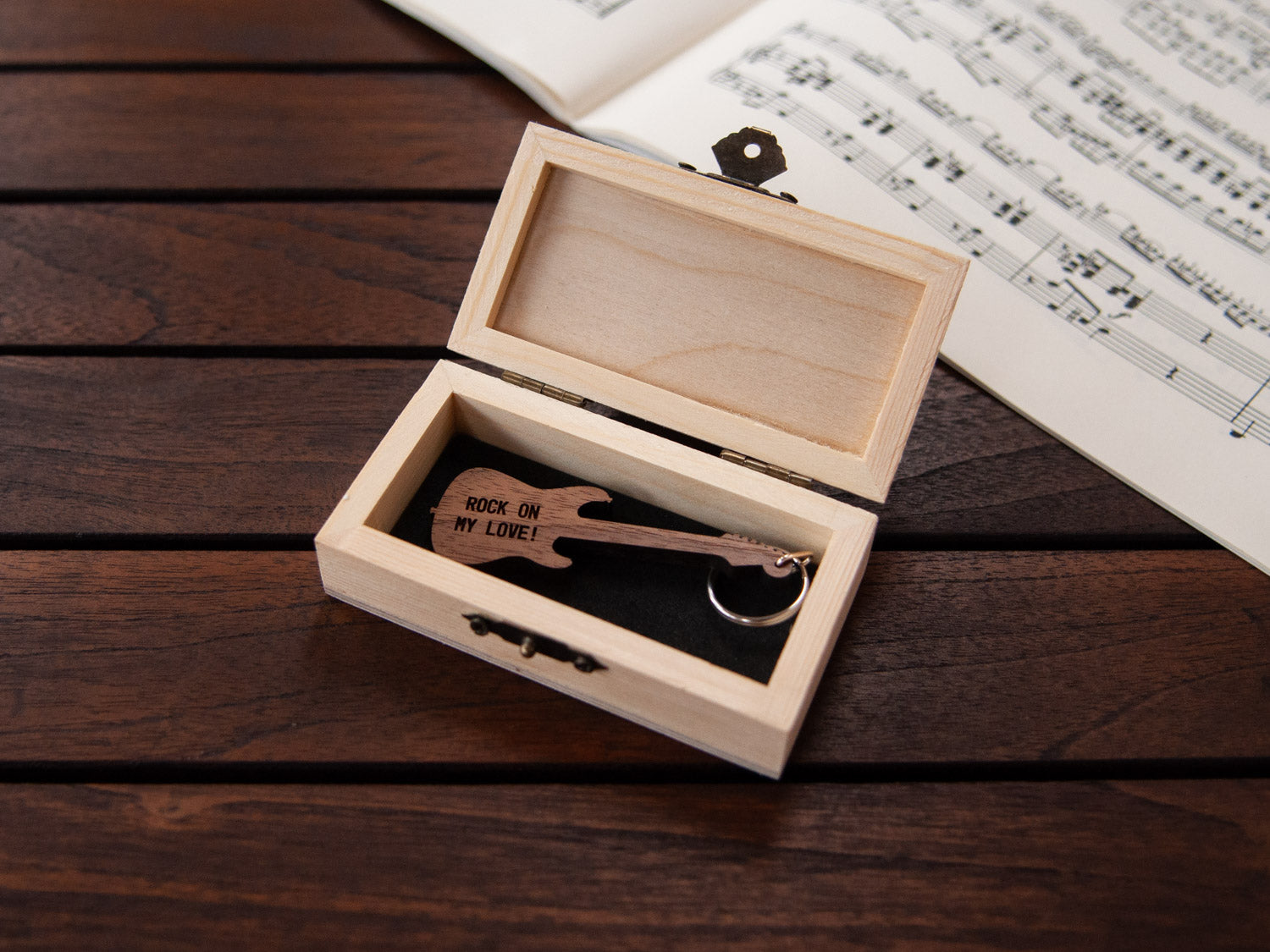 Electric guitar shaped keychain placed inside a compact wooden box, featuring a custom engraving.