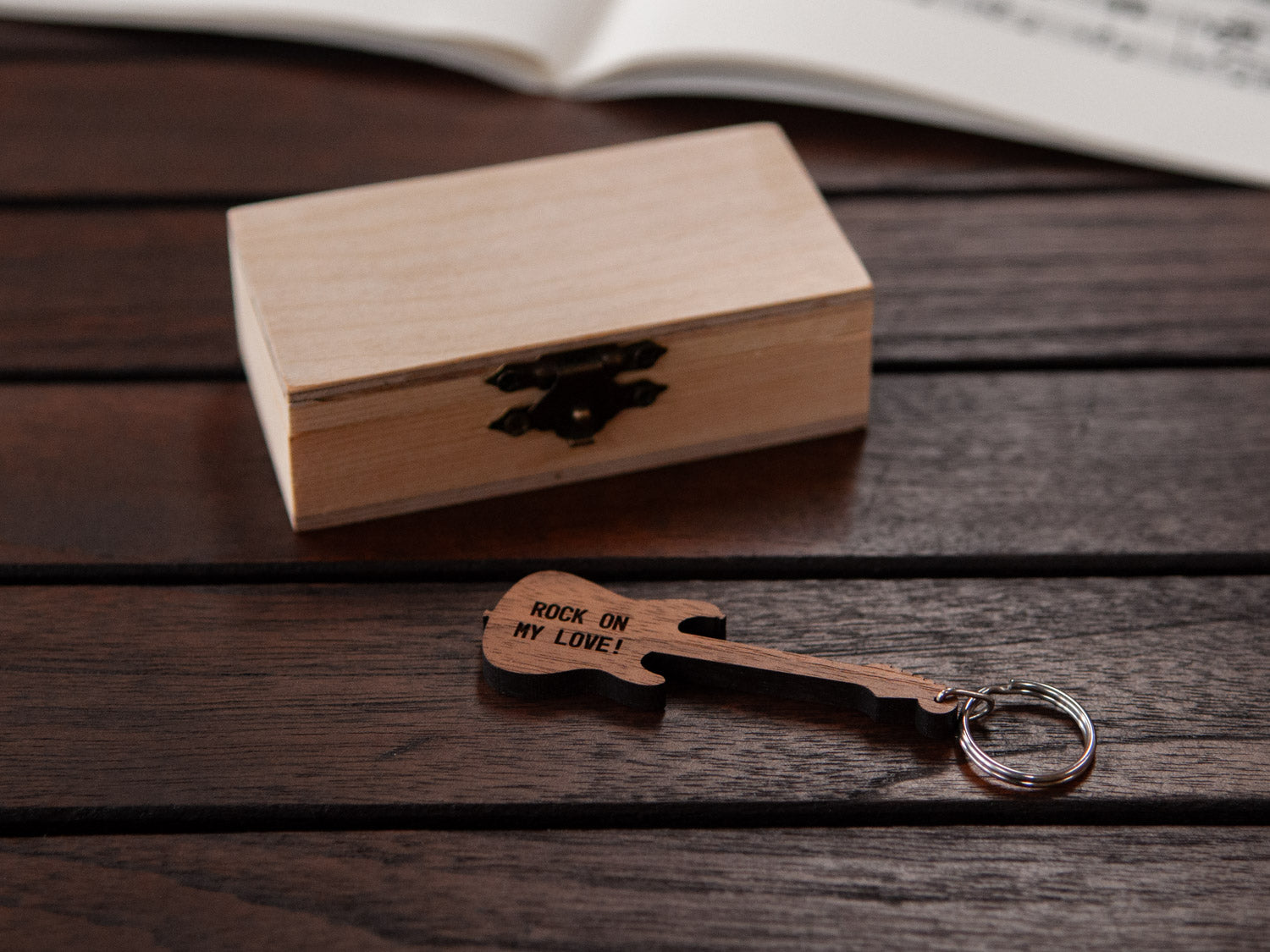 A guitar keychain with personalized text positioned in front of a small wooden box.