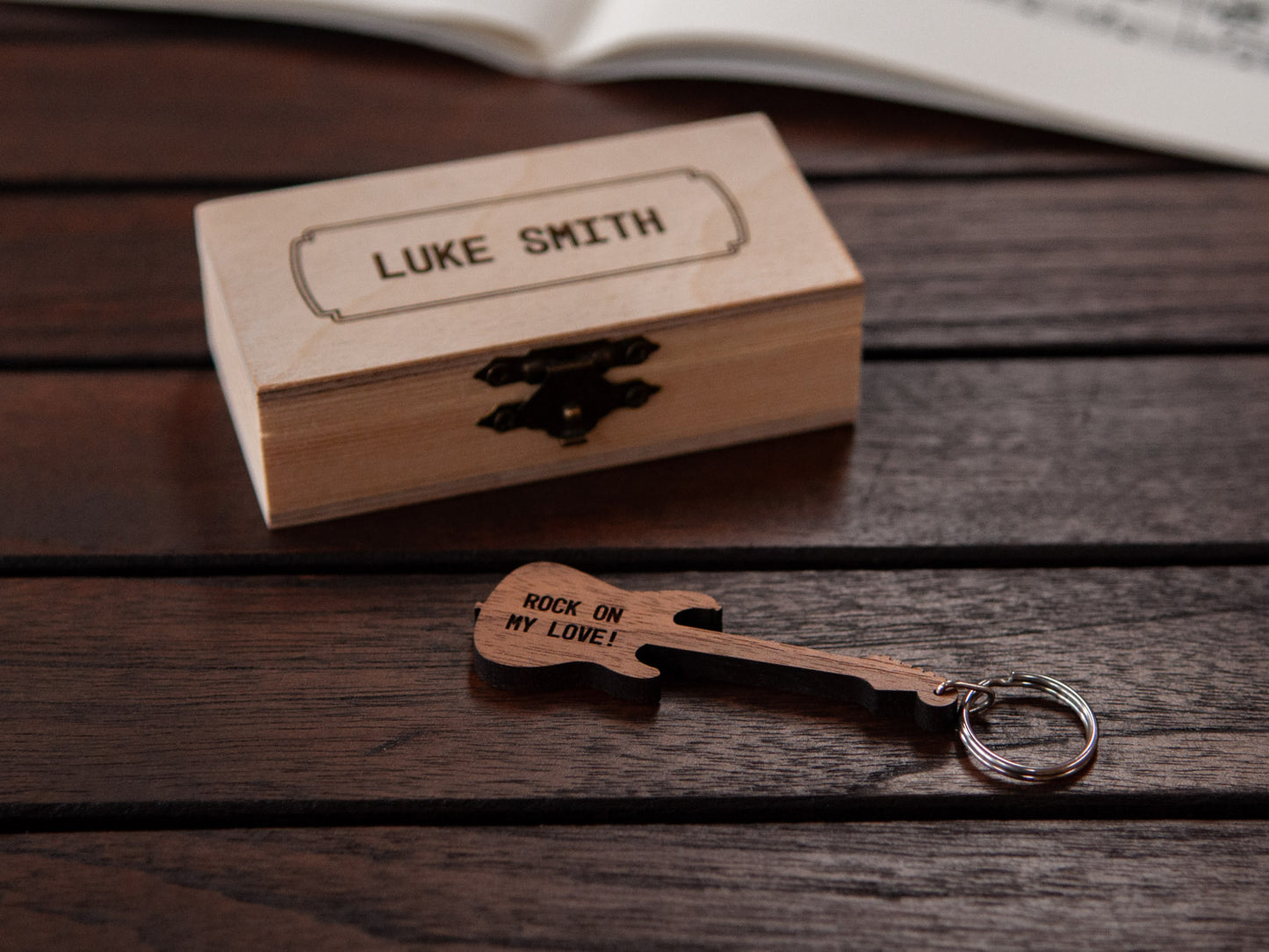 Electric guitar keychain displayed in front of a small wooden box, with a custom engraving.