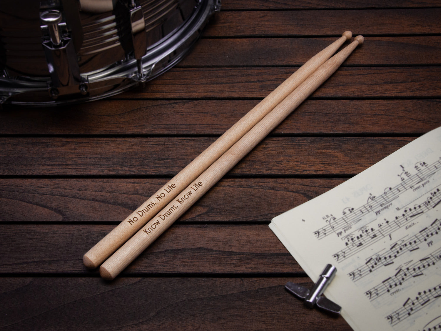 engraved drumsticks made from maple wood, placed on a table with an drum and sheet music on it