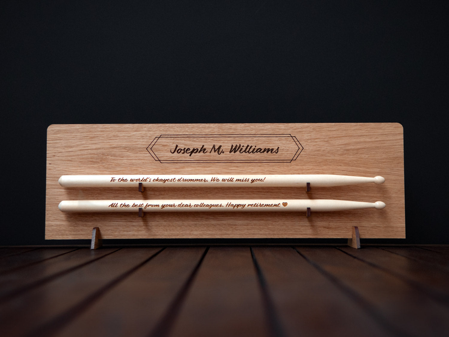 wooden drumsticks with an engraved message on them, placed on a light wooden display with an engraved name on it