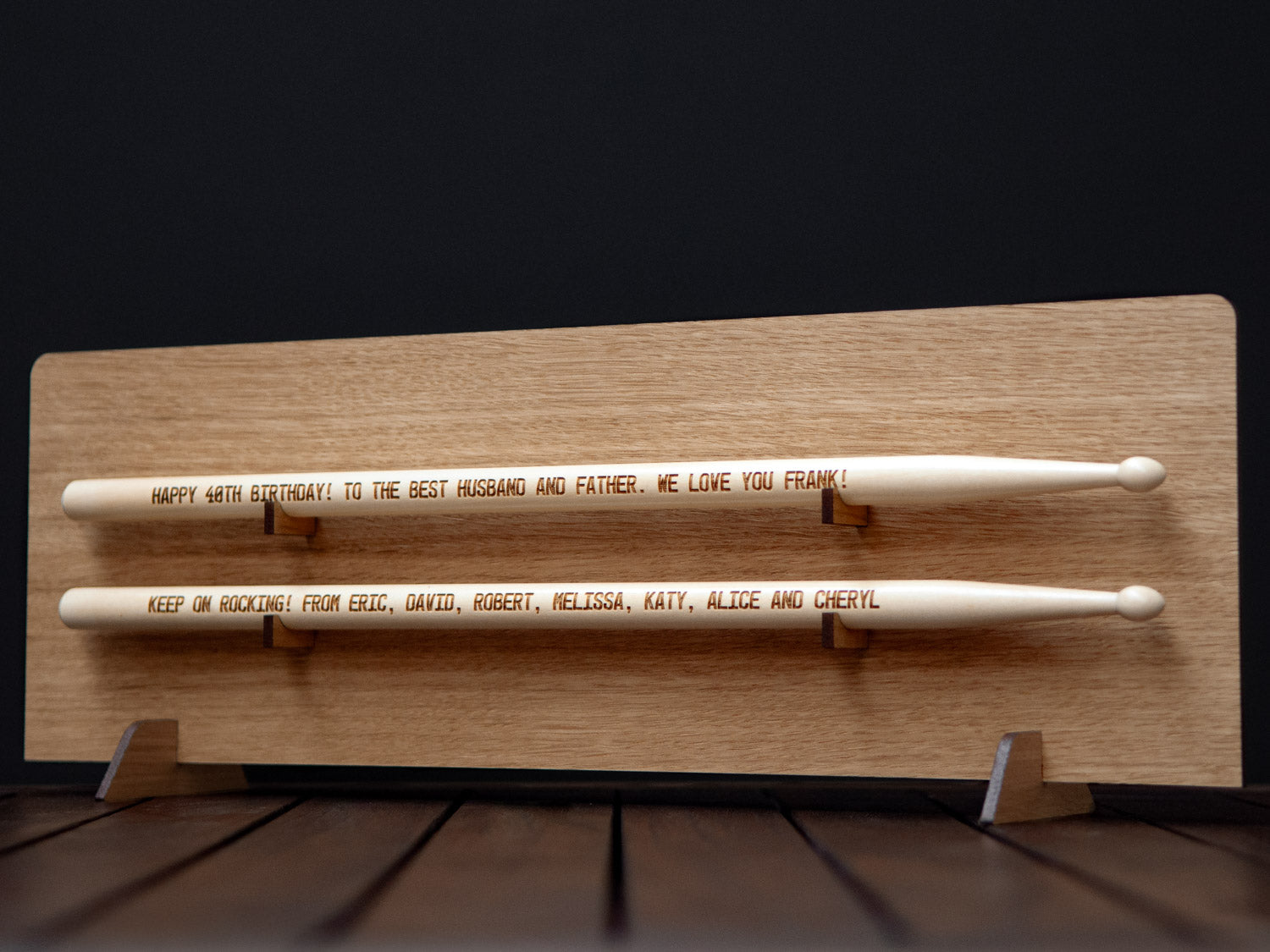 wooden drumsticks with an engraved message on them, placed on a light wooden display