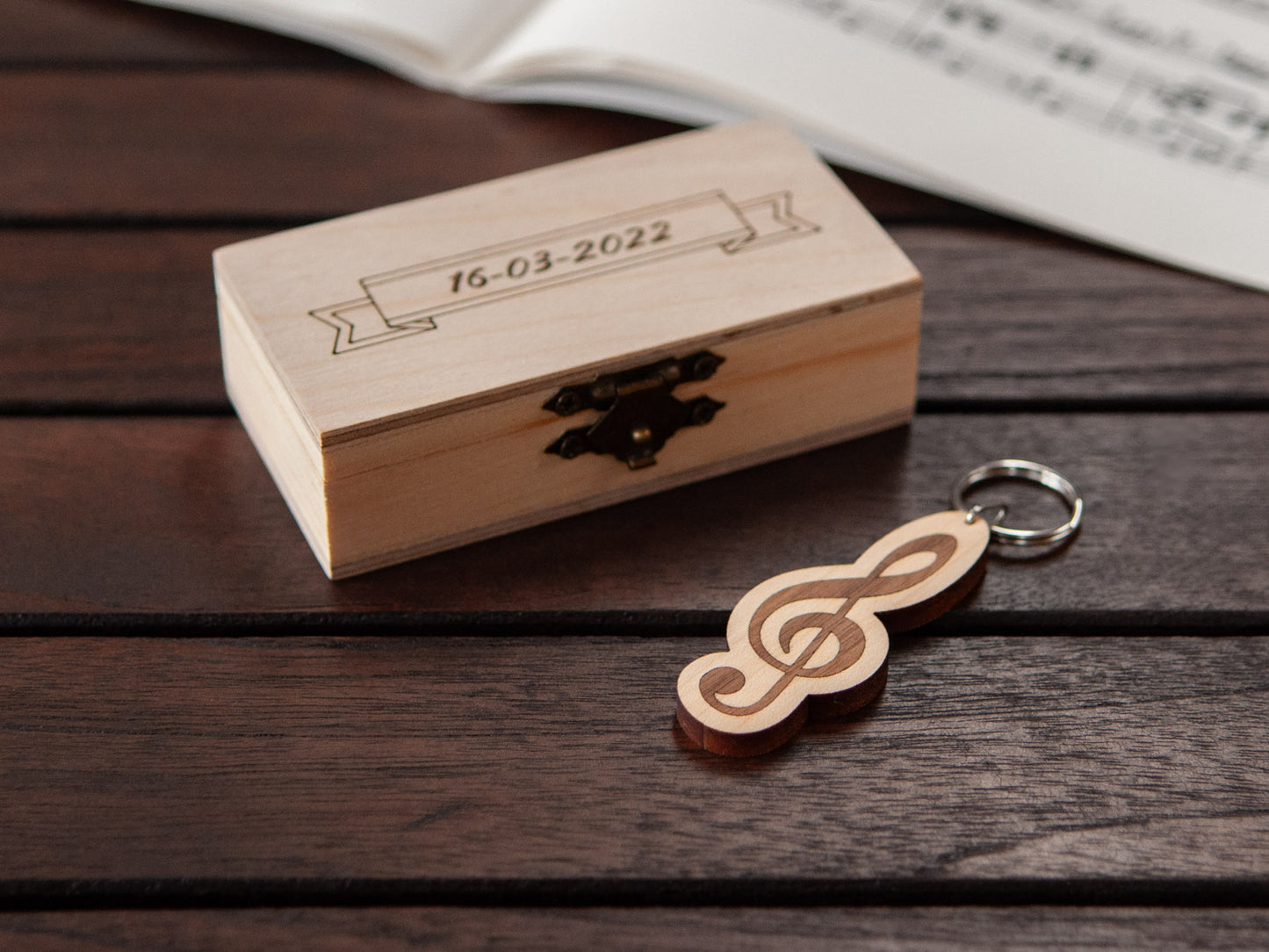 G-clef keychain displayed in front of a small wooden box, with a custom engraving.