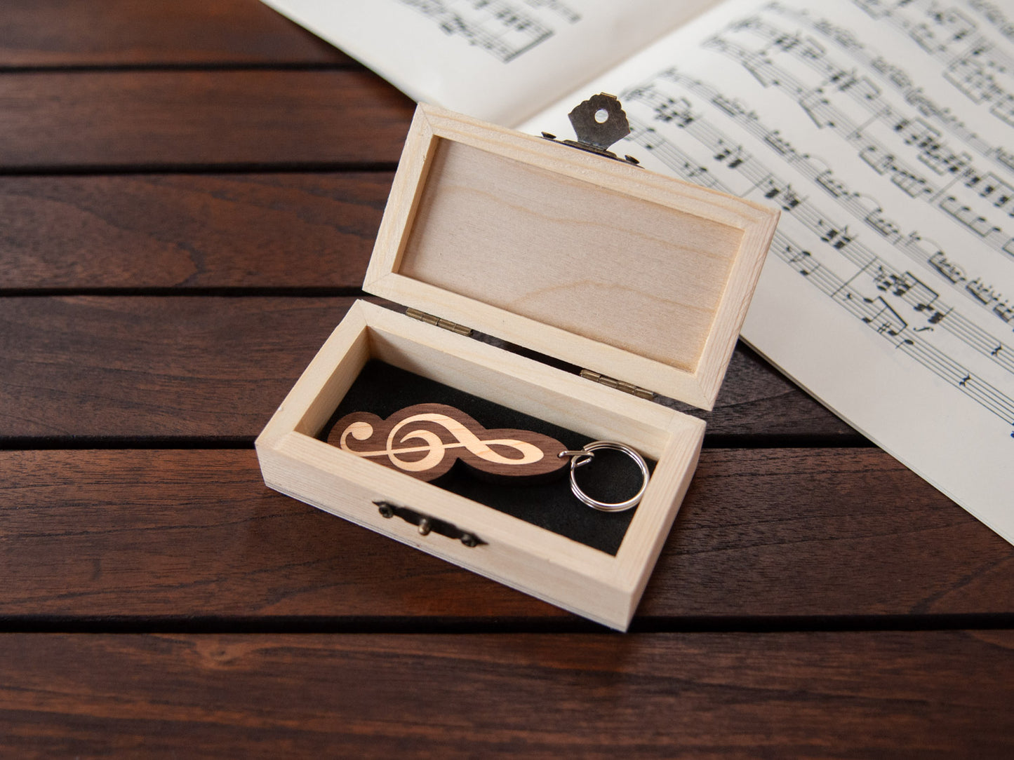 A G-clef shaped keychain placed inside a compact wooden box, featuring a custom engraving.