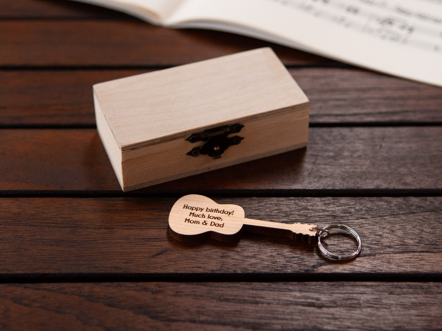 An engraved guitar keychain positioned in front of a small wooden box.