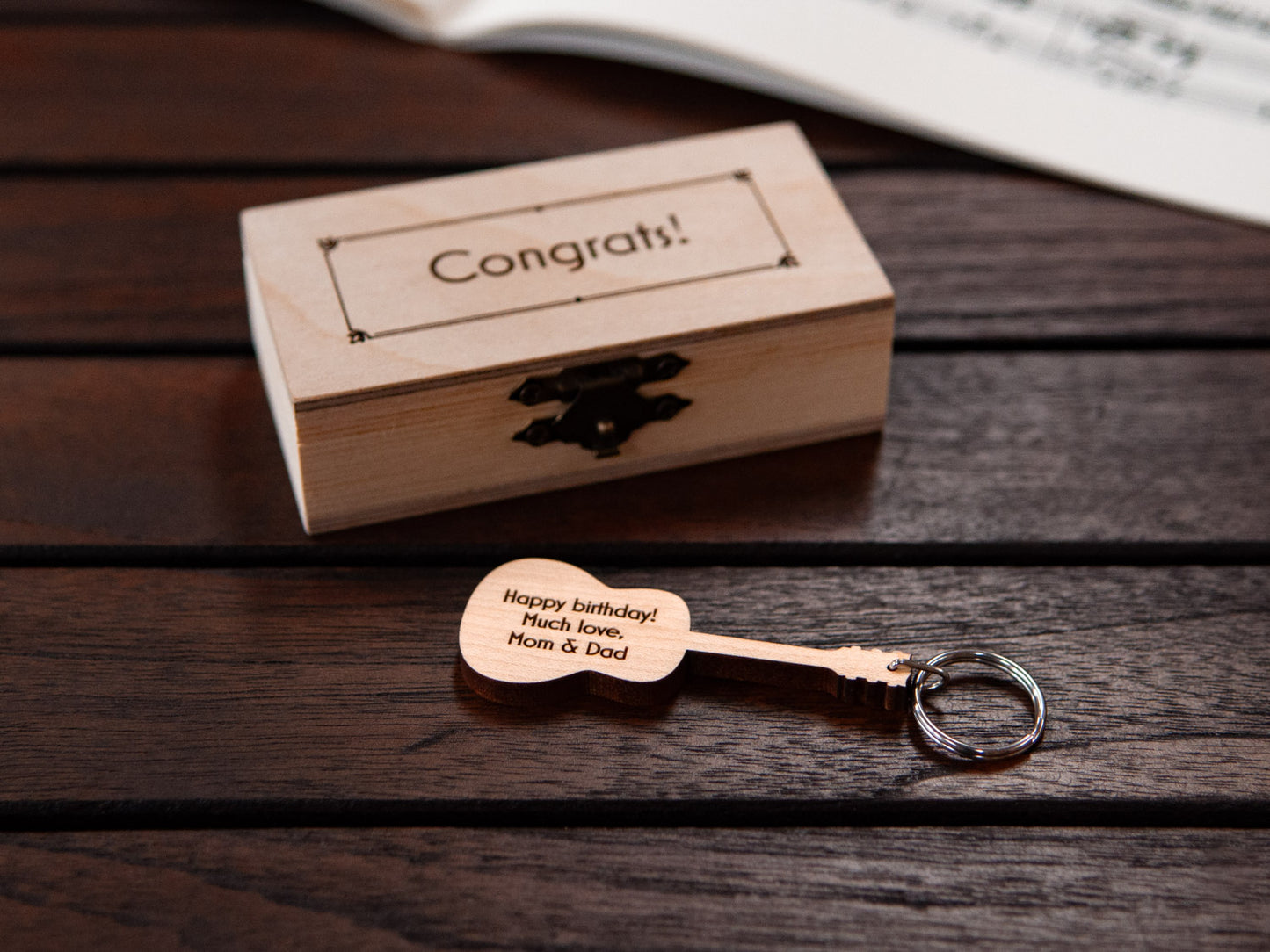 Guitar keychain displayed in front of a small wooden box, both with a custom engraving.