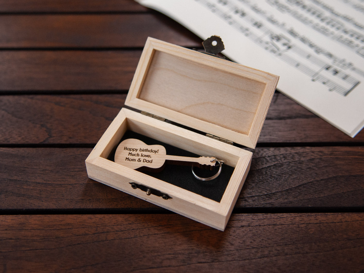 A guitar shaped keychain placed inside a compact wooden box, featuring a custom engraving.