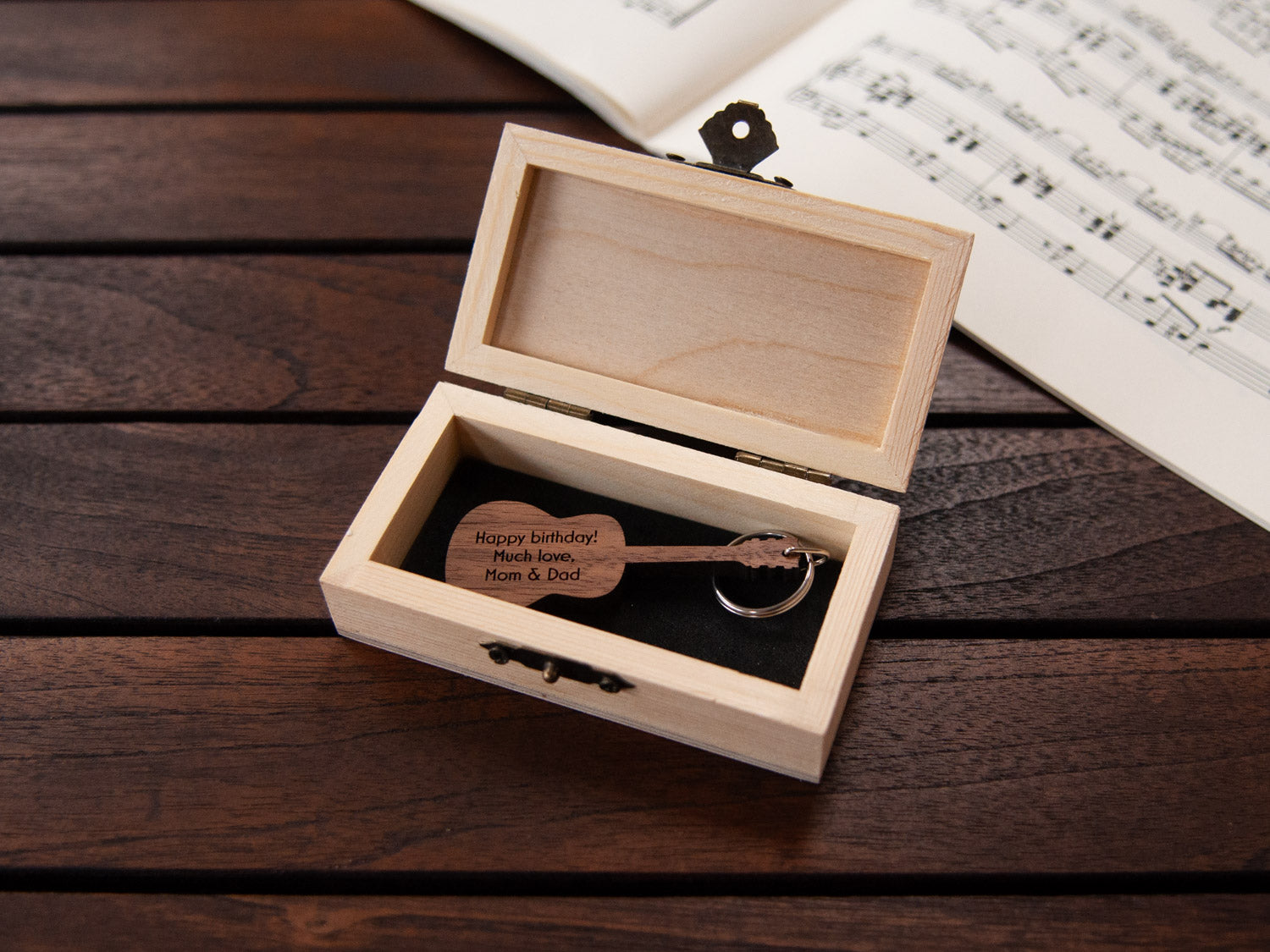 A guitar shaped keychain placed inside a compact wooden box, featuring a custom engraving.