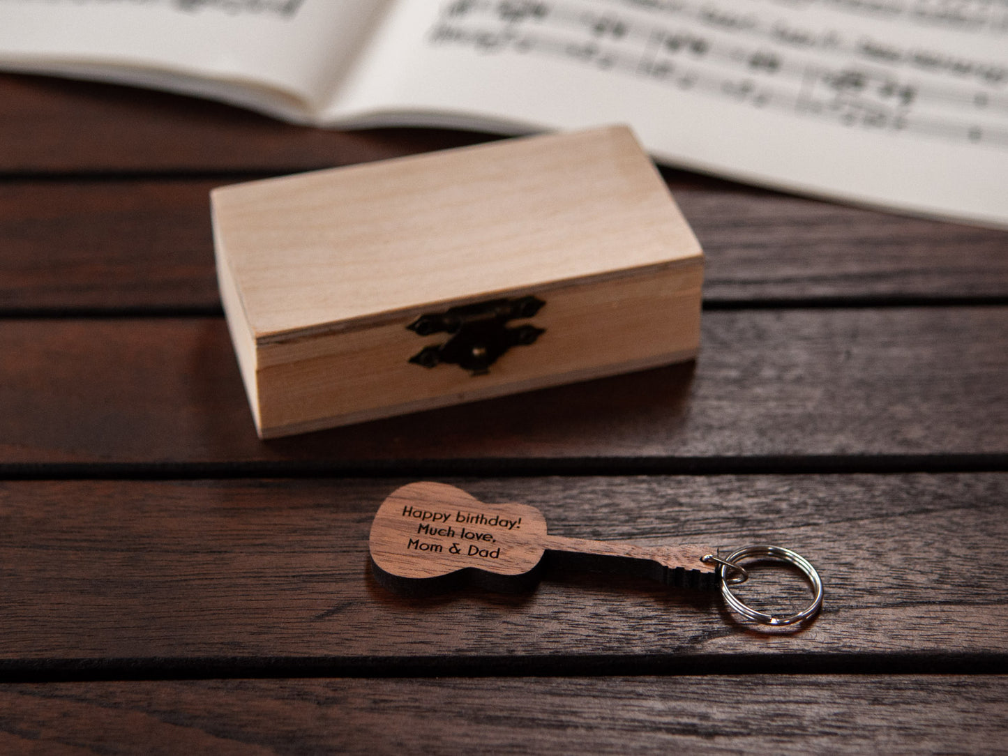 An engraved guitar keychain positioned in front of a small wooden box.