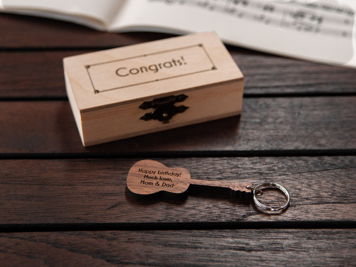 Guitar keychain displayed in front of a small wooden box, both with a custom engraving.