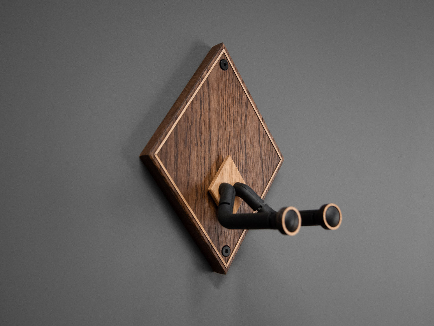 Side view of a wooden guitar wall mount in a diamond shape. The body is made from darkened oak, with contrasting light oak strips on the border