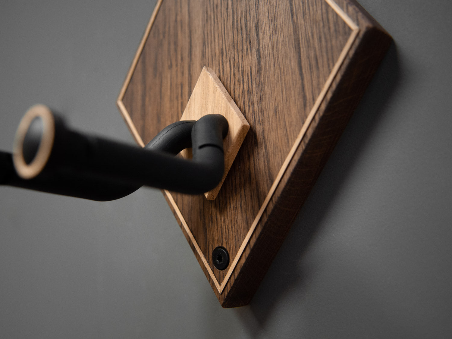 Details of a wooden guitar wall mount in a diamond shape. The body is made from darkened oak, with contrasting light oak strips on the border