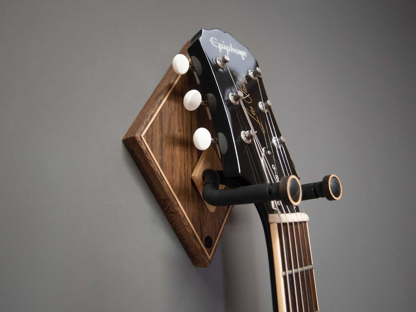 A black guitar hung on a dark wooden guitar wall mount