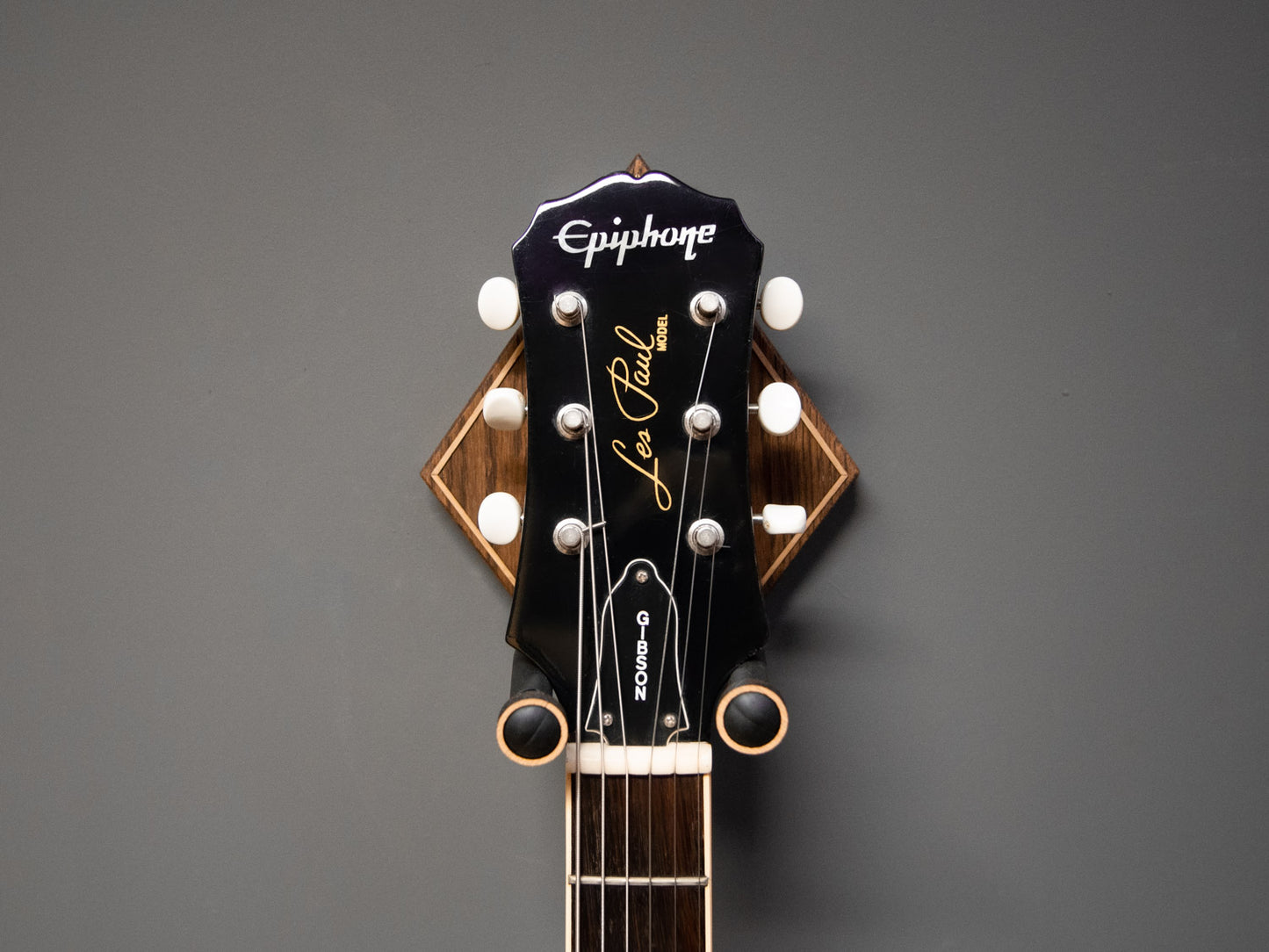 Front view of a guitar neck, hung on a dark oak wall mount, with light oak details