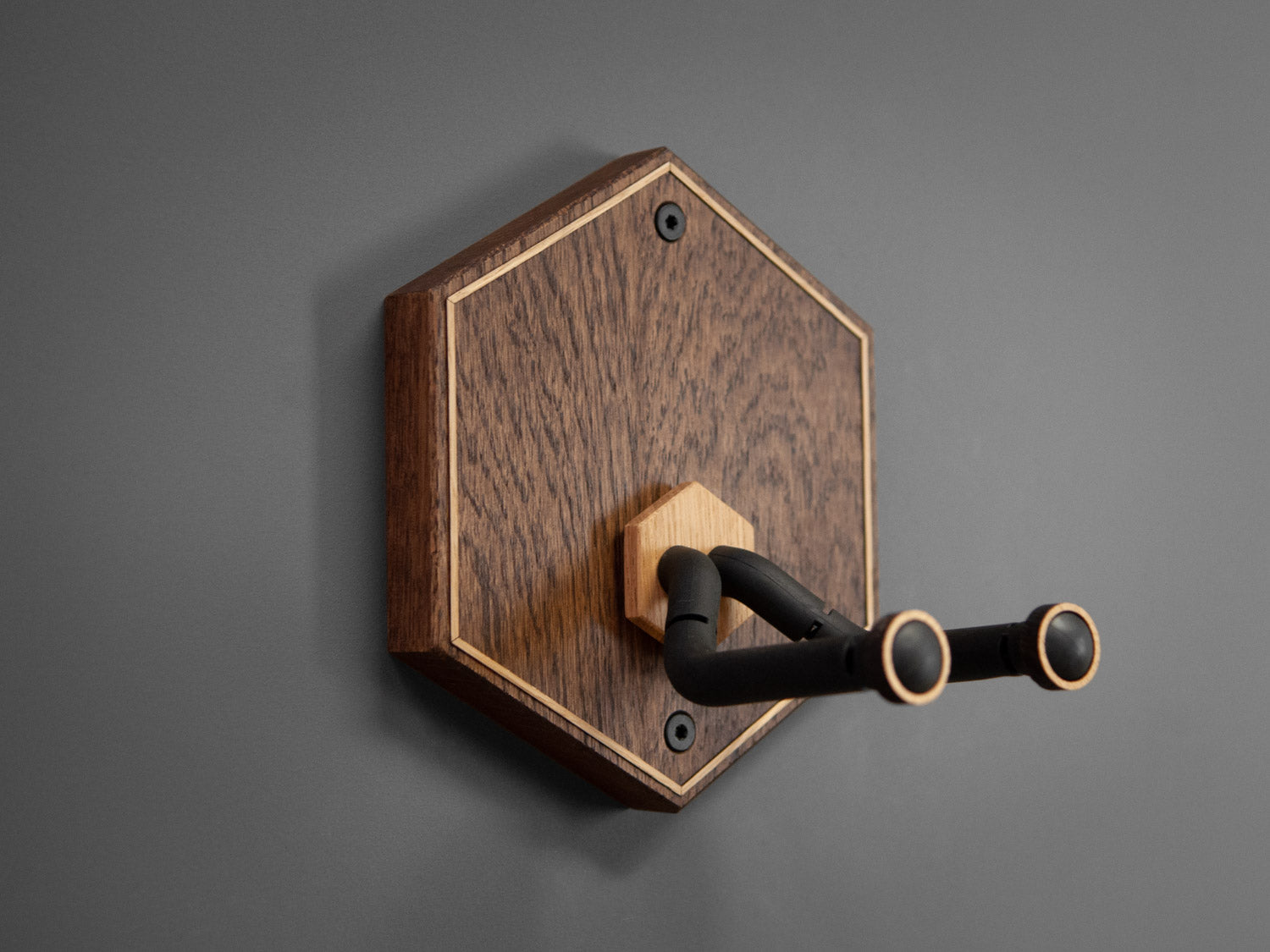 Side view of a guitar wall mount in the shape of a hexagon. The body is made from darkened oak wood, with contrasting light oak strips